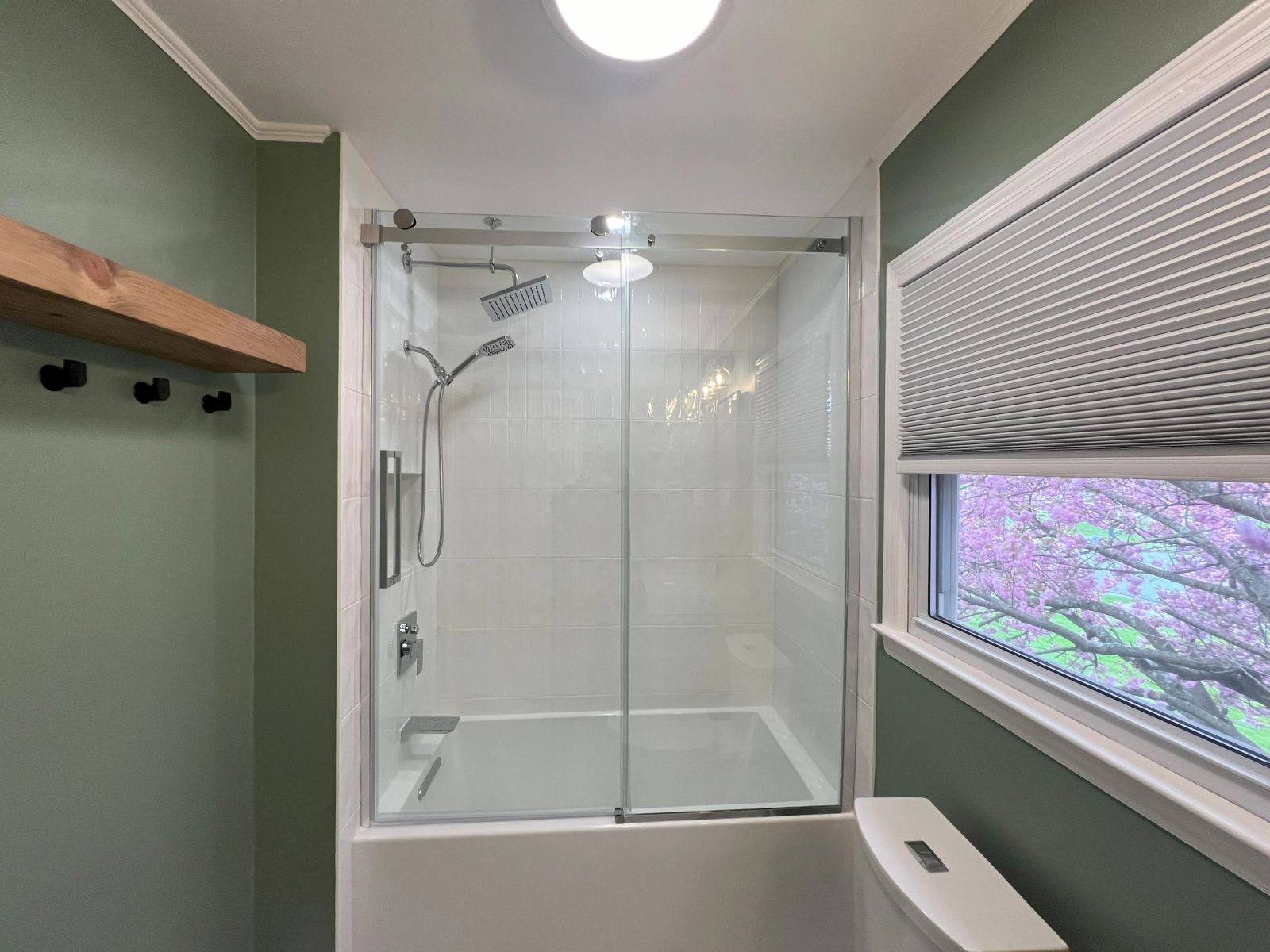 Tub and shower combination with sliding glass door, floating wood shelf and matte black fixtures