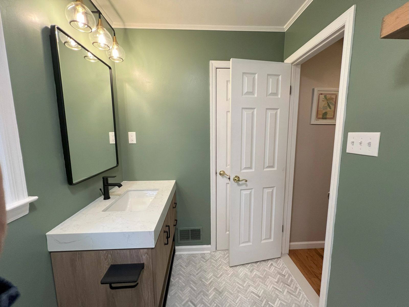 Bathroom with floating wood vanity, black framed mirror, sage green walls and herringbone tile floor