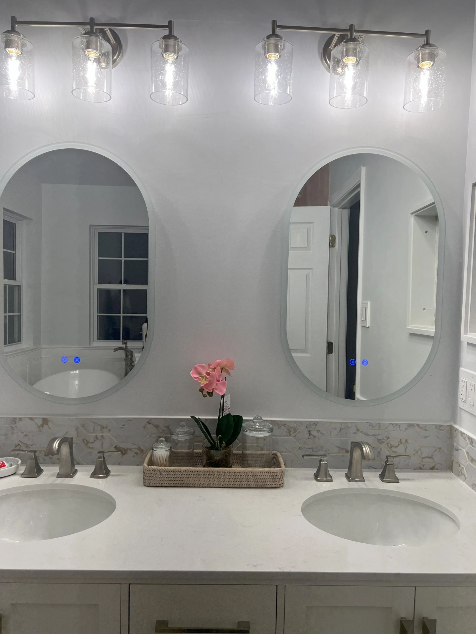 Double vanity with two oval mirrors and six glass globe light fixtures above a stone-look countertop
