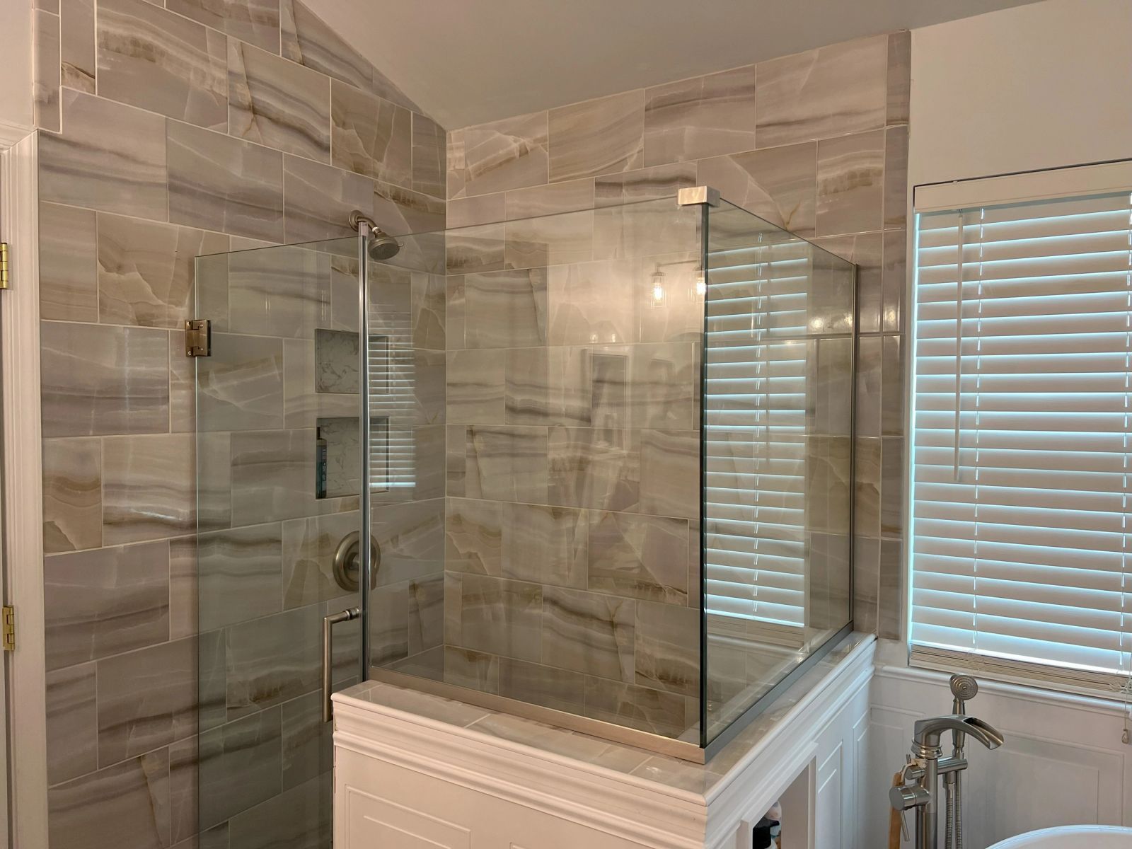 Walk-in shower finished in large-format marble-look tile with frameless glass panels and white wainscoting