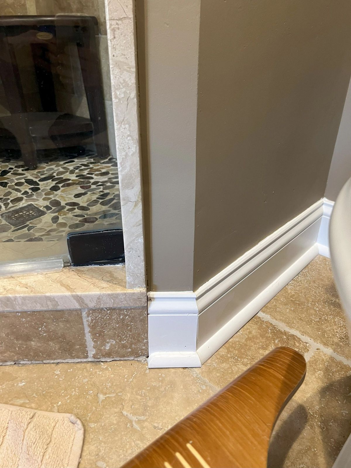 Newly installed white baseboard trim meeting a stone tile floor