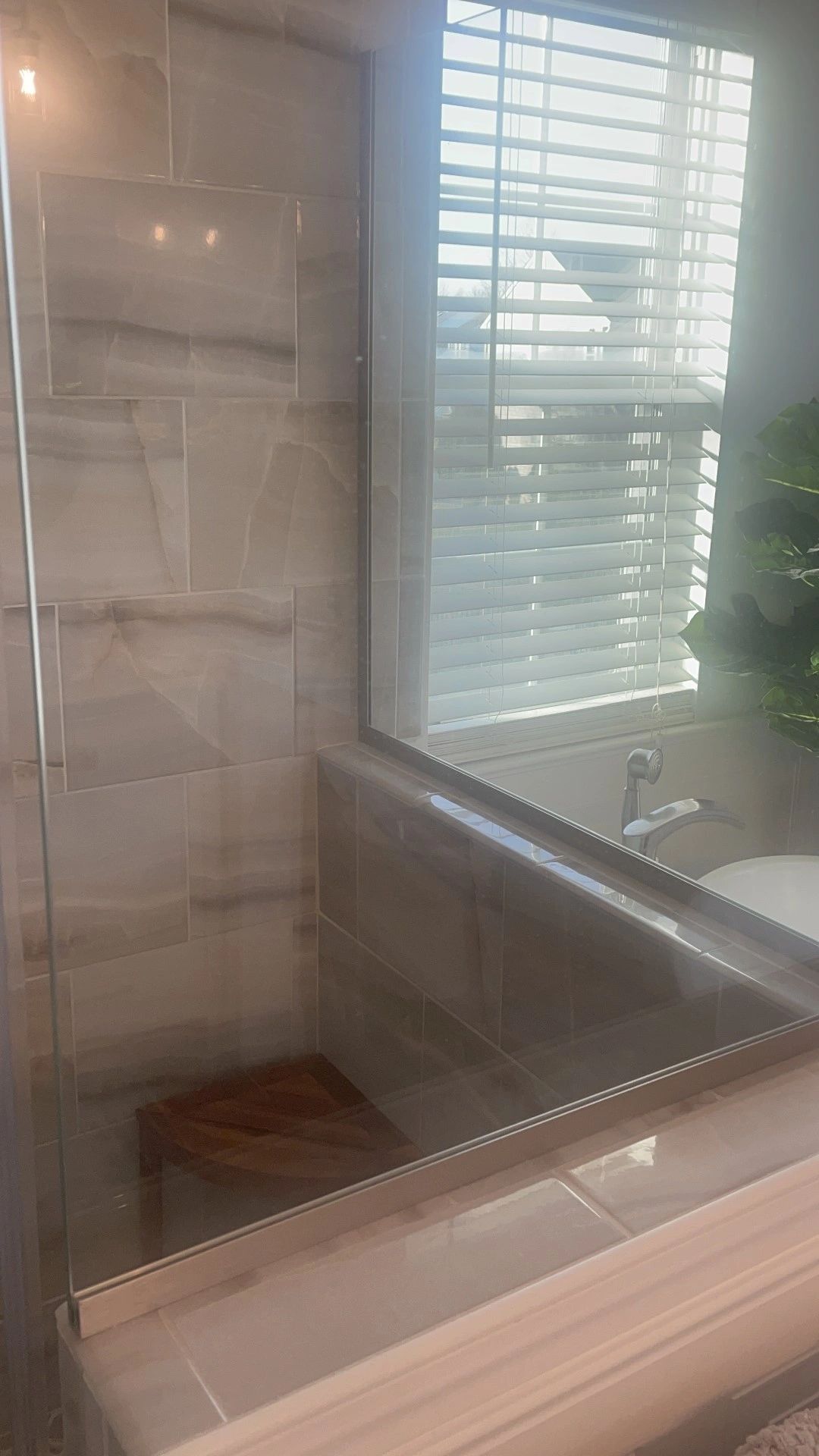 Tub surround tiled in large-format marble-look tile up to the window